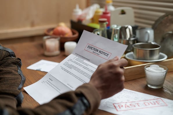 A man reading an eviction notice at a table next to a past due paper
