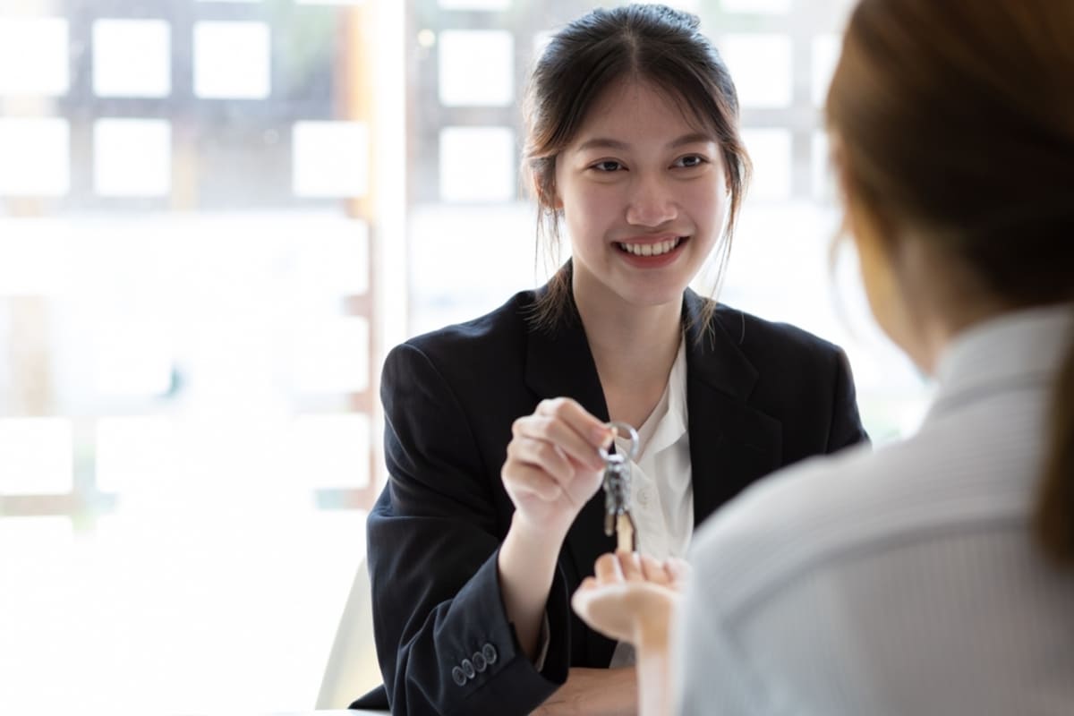 A woman in a suit handing keys to someone.