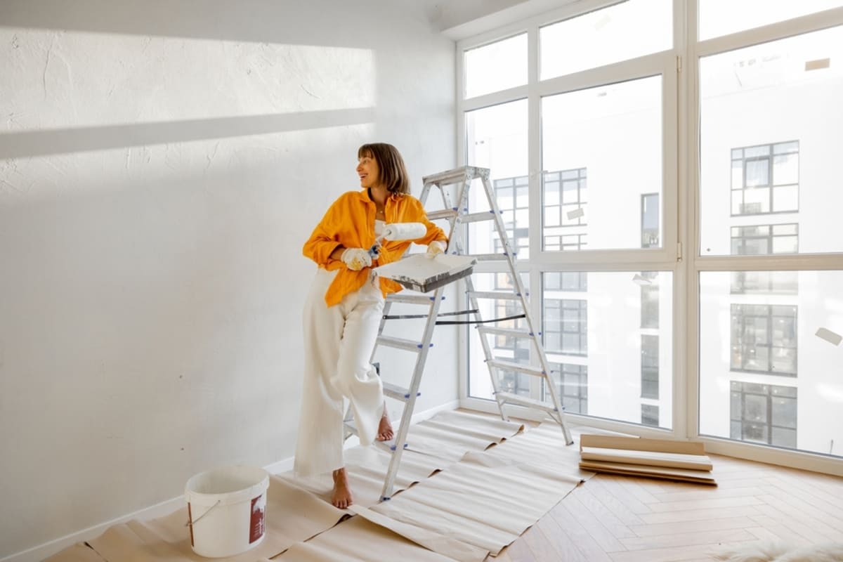 A woman painting the wall white and leaning on a ladder