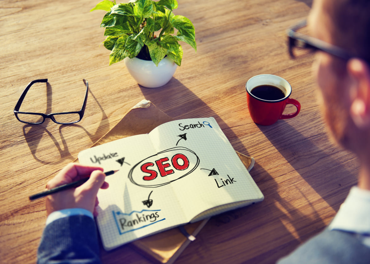 An open notebook that says SEO next to a cup of coffee and glasses