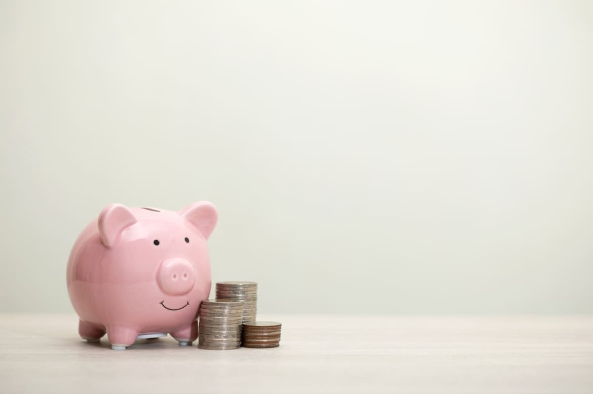 Stacked coins on a desk next to a piggy bank
