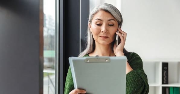 Woman on phone call reviewing property management interview questions on a clipboard