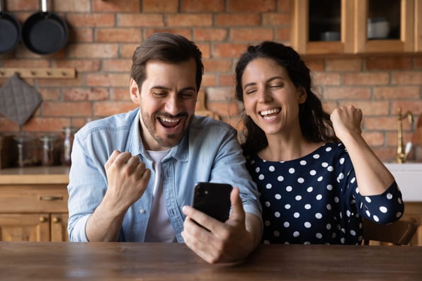 Two people cheering while looking at their phone