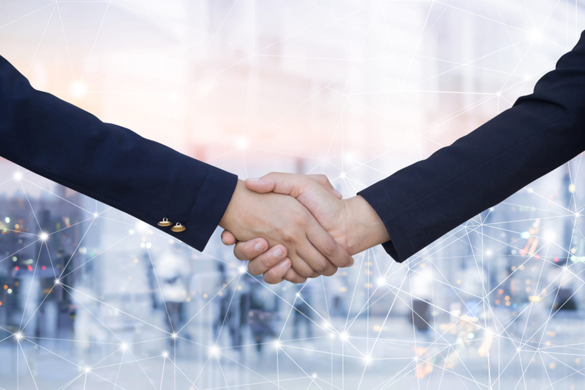 Two people in suits shaking hands in front of a web background