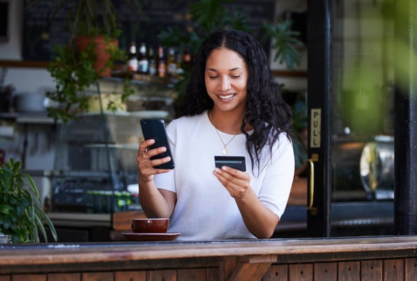 Young woman holding a credit card uses her phone to pay rent