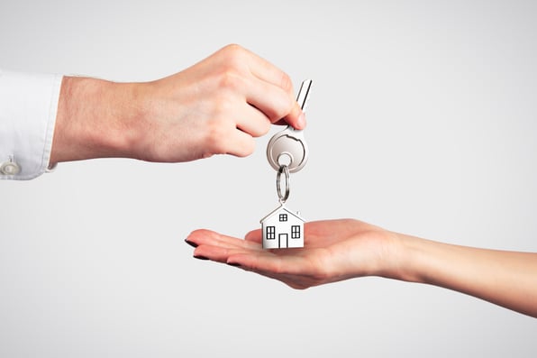 A hand holding a house key over an open palm with a small house keychain, symbolizing the transfer or inheritance of a property.