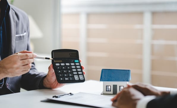 Real estate agent pointing at a calculator next to a small model home