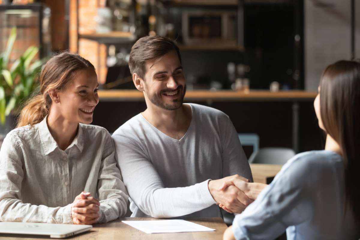 A property manager shakes hands with a young couple, tenant screening concept