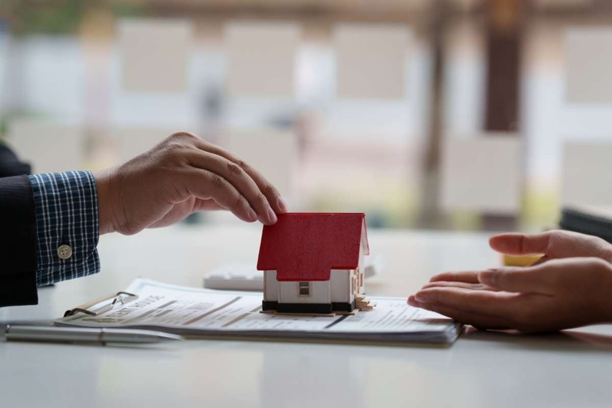 Close-up of hands and a model house on a table, Hampton property management concept. 