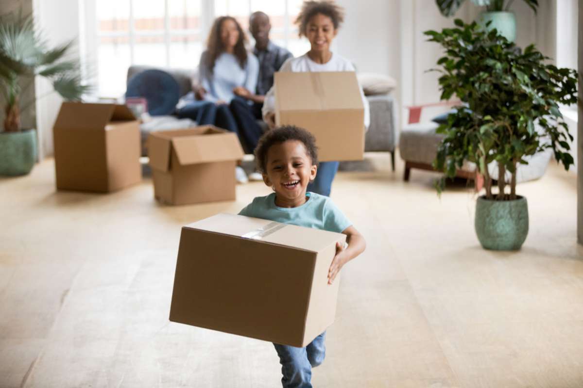 Cute happy mixed race children enjoying moving day running carrying holding boxes