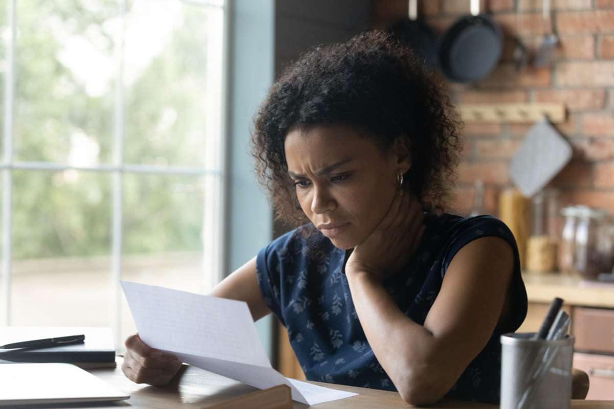 Frustrated young african american woman reading paper letter with bad news
