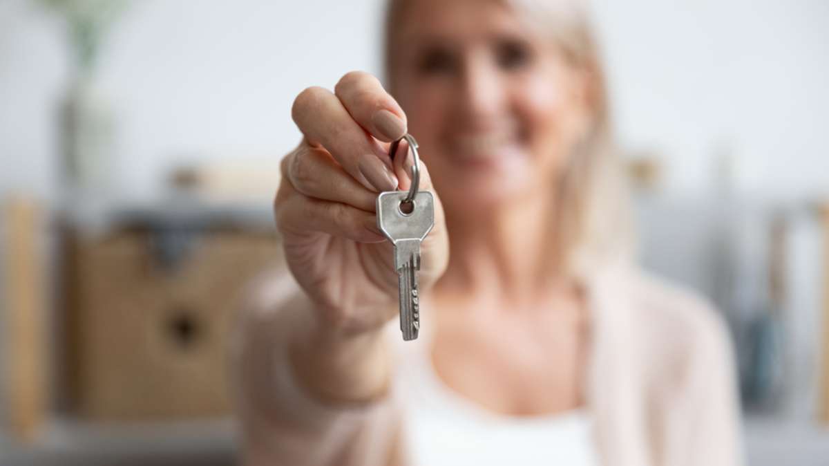 Happy senior middle aged woman customer landlord hold key to new house apartment give to camera