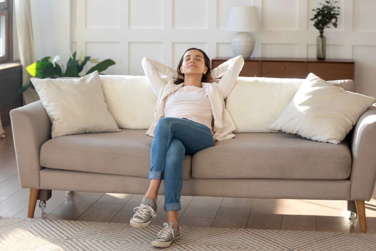 Happy serene young female relaxing on couch at living room leaning back on pillows
