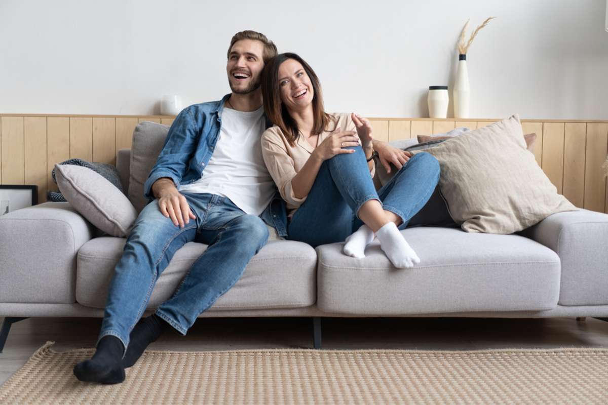 Happy couple relaxes on a cozy sofa at home as happy tenants from excellent rental property maintenance services.