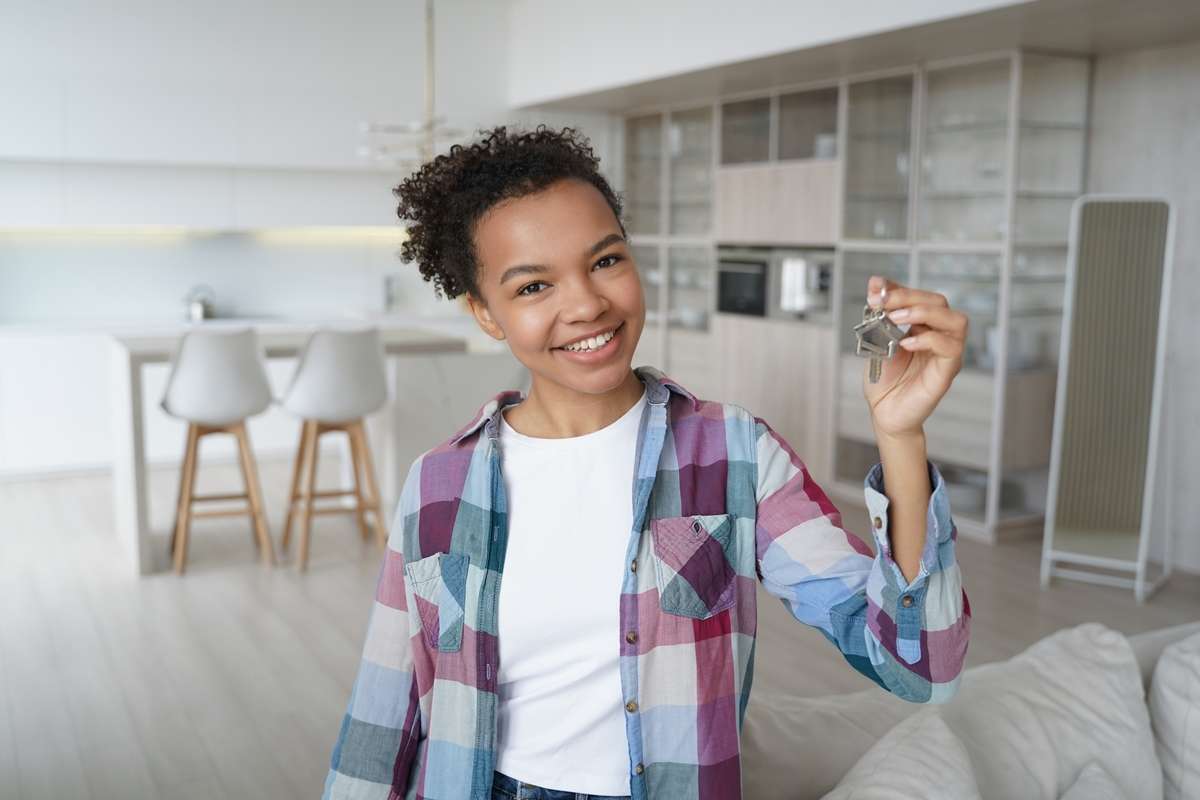 Happy young biracial girl homeowner tenant shows key to new house