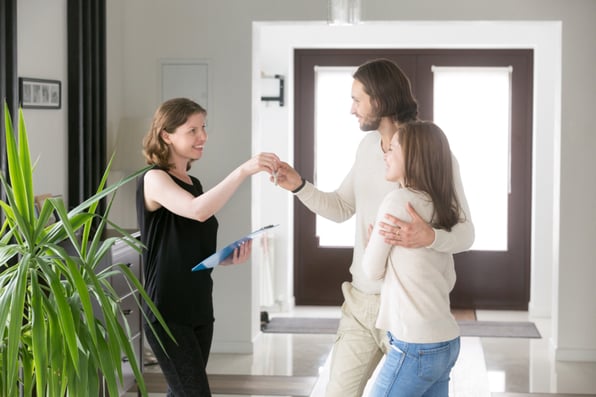 Happy young married couple hugging and receiving house keys from realtor