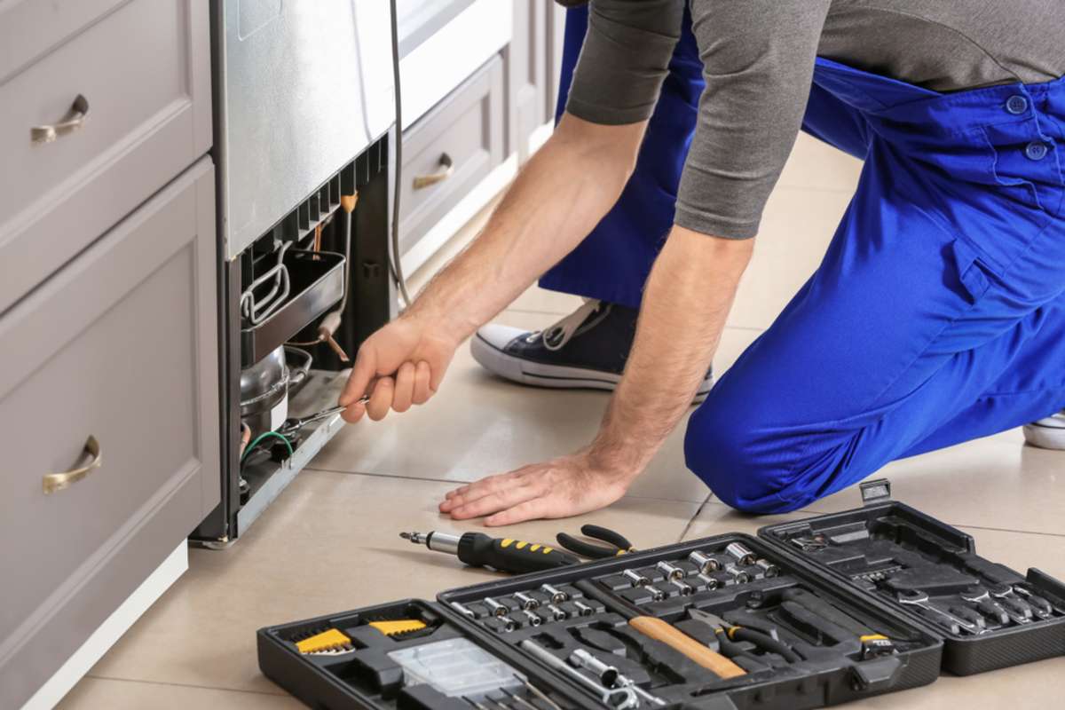 Technician repairing refrigerator indoors, rental property maintenance services concept. 
