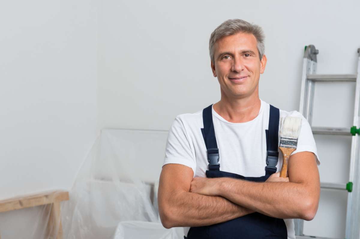 Portrait Of Smiling Painter With Arm Crossed Holding Paintbrush At Home