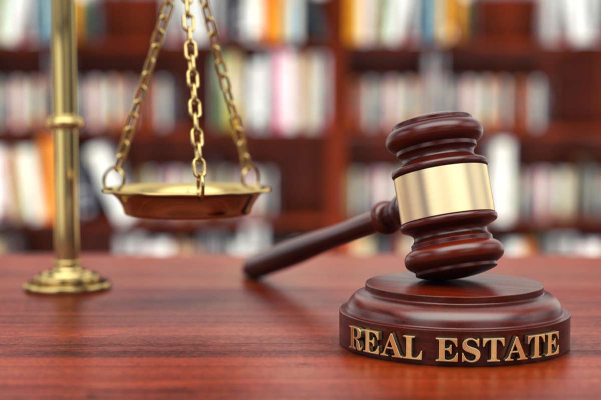 A gavel that says real estate next to a scale