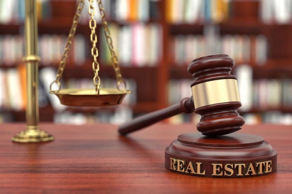 A gavel that says real estate next to a scale
