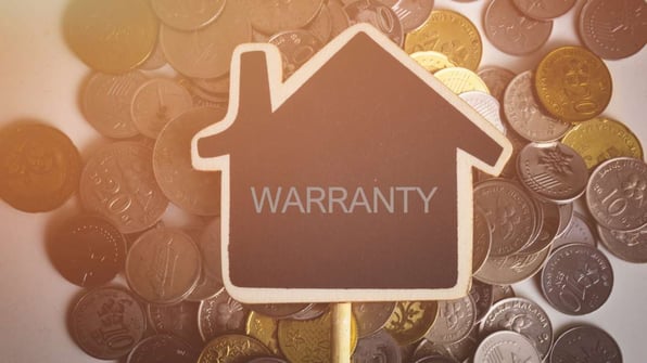 A sign in the shape of a house that says warranty on top of coins