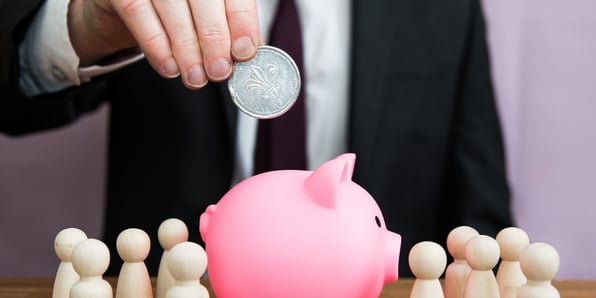 A man in a suit putting a coin in a piggy bank.